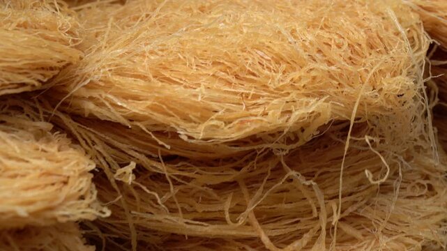 Raw kataifi dough stacked and ready for baking traditional middle eastern desserts like kunafa, a detailed close-up showing the fine texture of the phyllo pastry
