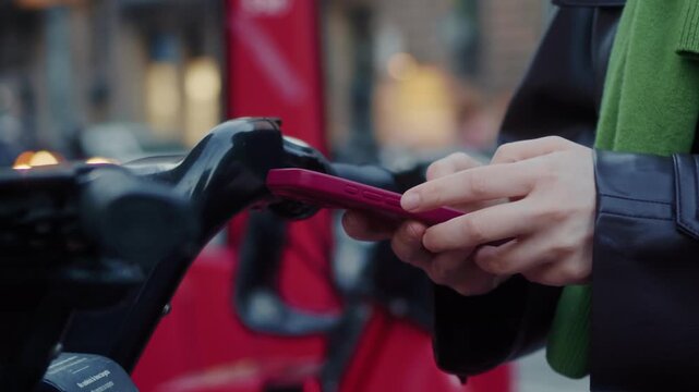 A close-up of hands using a smartphone with a bike-sharing app near a city bike rack. Concept of urban mobility, shared-ride services, and transportation. High quality 4k footage