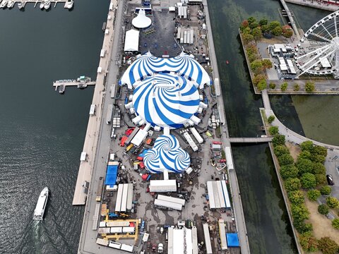 24th of August 2025 drone flight above the Cirque du Soleil blue-white tent at Montreal Old Port with city skyline in background. g.