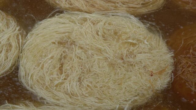 Close-up of traditional kadayıf dessert, a turkish sweet pastry, deep frying in sizzling hot oil, demonstrating the authentic preparation of this middle eastern delicacy