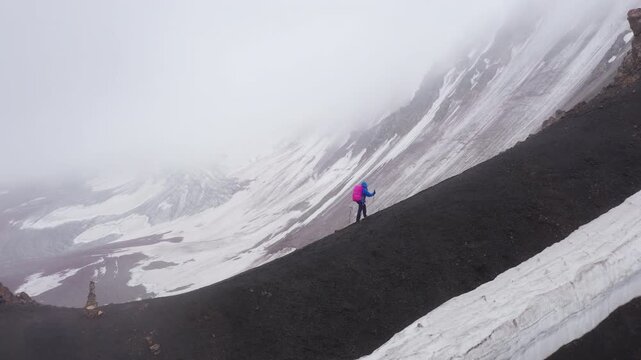 Lonely female backpacker in a rain cover with a backpack and trekking poles, making an acclimatization trek around Lenin Peak base camp and climbing Petrovsky Peak (4910 m) Pamir mountain, Kyrgystan