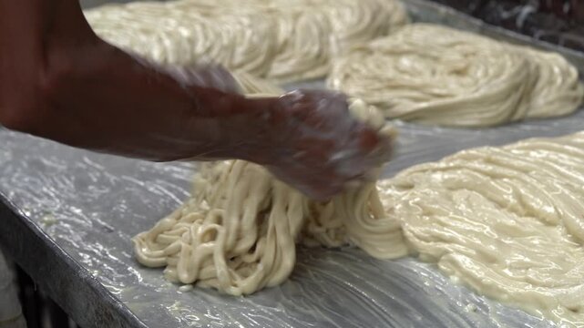 Street food worker skillfully preparing long strands of raw sutarfeni dough for deep frying, showcasing a traditional indian sweet making culinary technique