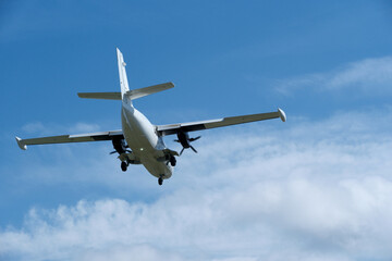 Obraz premium Twin-engine short-range transport aircraft on final approach to landing in blue sky with clouds. Regional twin-prop airplane landing in bright blue sky with fluffy clouds