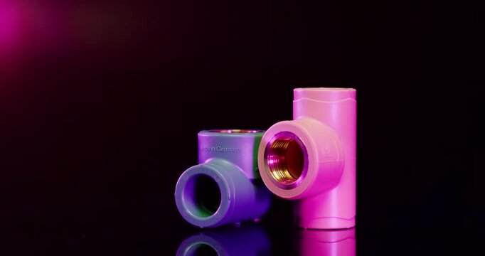 Blue and pink plastic T-joint pipe fittings with metal screw threads on dark background with red light