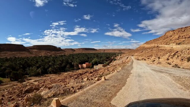 Driving through ziz valley revealing a lush green palm oasis and traditional village in moroccan desert landscape