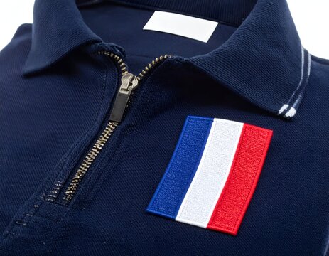 Close-up of a blue polo shirt with zipper, white collar tag, and French flag patch