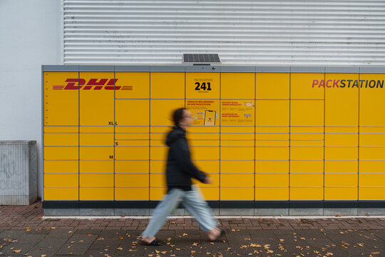 Dusseldorf, Germany - September 10 2025: DHL Packstation parcel lockers with motion blur pedestrian passing in front of units