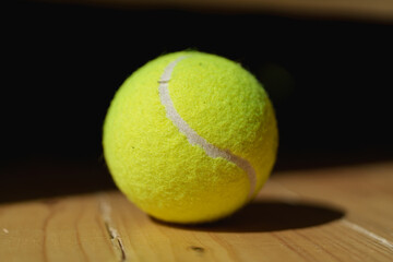 Close up of yellow tennis ball on a wooden floor with hard lighting