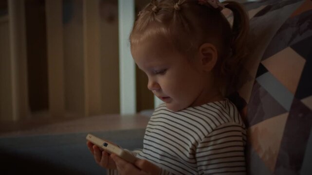 Young child engrossed colorful cartoons smartphone screen, snuggled on sofa evening, sparks worries about gadget addiction potential risks to their eyesight overall health due to excessive screen time