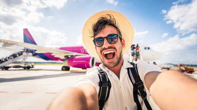 Happy tourist boarding on a plane at the airport - Handsome young man taking selfie picture in front of airplane