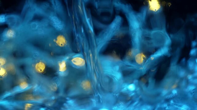 Defocused blurred bokeh background of blue fibrous liquid texture with glowing golden light spots. Concepts for holiday design, beauty and cosmetology, advertising posters, mineral water packaging