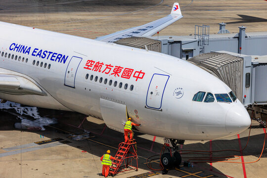 Shanghai, China - 2026 August 11: Two ground crew members performing pre-flight checks or maintenance at the front hatch of a China Eastern Airlines Airbus A330 at Shanghai Pudong 