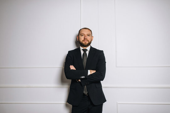 Photograph of a stylish mature businessman in a suit and tie standing against a white wall in his office. Business concept.