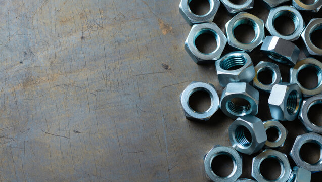 A cluster of chrome-plated hexagonal steel nuts on a scratched industrial metal background. Clean engineering composition with text space for Labor Day concept, and industrial holiday promotions