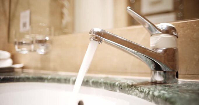 A steady stream of water flows from a sleek silver faucet into a green marble vanity sink. Close up shot, real time video