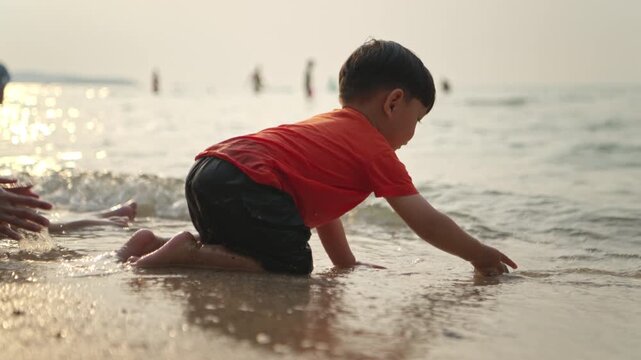 The little child sits on the beach at sunset, throwing stones while their mother and father sit beside them