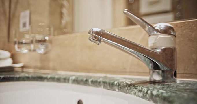 Modern chrome lever tap dripping water into a green marble vanity sink in a bathroom. Close up shot, shallow depth of field, real time video