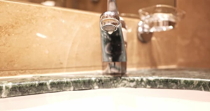 Modern chrome lever tap dripping water into a green marble vanity sink in a bathroom. Close up shot, shallow depth of field, real time video
