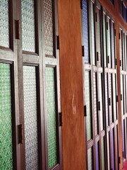 Obraz premium A perspective view along a row of traditional Thai-style folding windows with multi-colored glass panes and rich wooden frames.