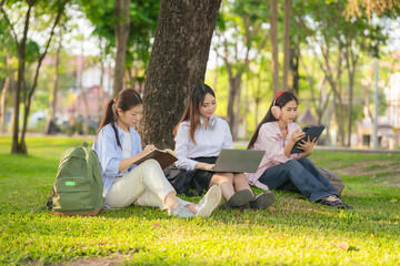 Naklejka premium Three young women are sitting together outdoors in what appears to be a park or campus. They are students relaxing or reading together outside.