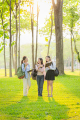 Fototapeta premium Three Asian schoolgirls with backpacks and tablets are on their way to or from class. A moment of social happiness.