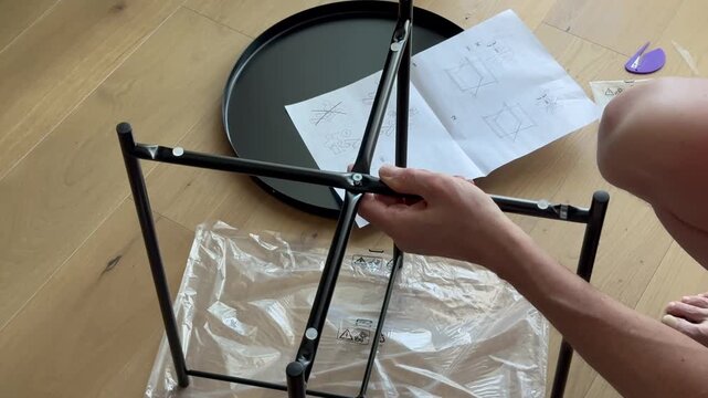 Hands assemble coffee table frame and tighten bolt using hex key on floor. Fingers fix metal parts following instruction during furniture setup. Concept diy, home, assembly, interior..