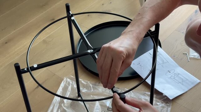 Hands assemble coffee table frame by connecting metal parts on floor. Fingers build structure following instruction during furniture setup. Concept diy, home, interior, assembly..