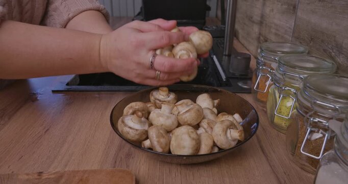 Woman's hands meticulously washing and cleaning fresh whole champignon mushrooms over a kitchen sink, preparing the raw, organic ingredients for a healthy homemade vegetarian meal.
