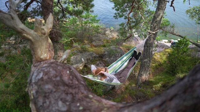 Couple relaxing in hammock by lake, authentic outdoor moment in wild nature, mental health and sustainable travel concept, natural light.