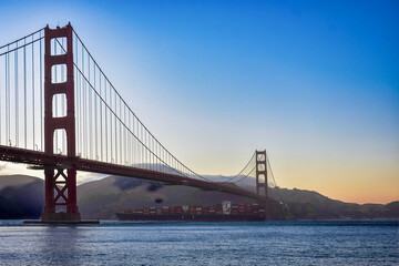 Obraz premium A cargo ship passing beneath the Golden Gate Bridge in San Francisco, California during a foggy Sunset