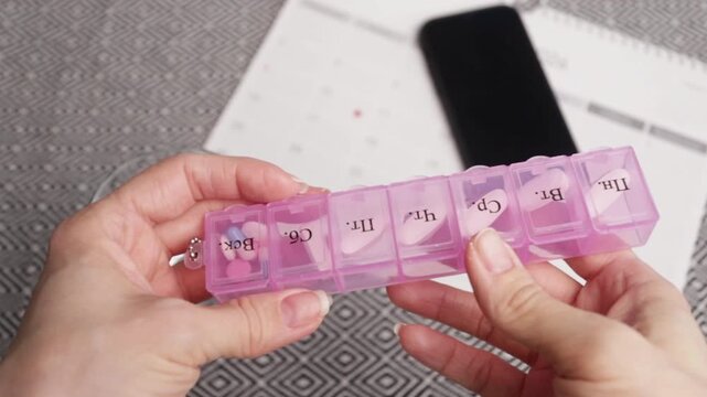 hands hold pill organizer with smartphone and calendar background, medication planning and reminders