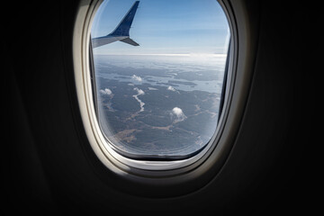 Fototapeta premium An aerial view through a commercial airplane window shows a vast archipelago of forested islands scattered across the blue sea under a clear sky.
