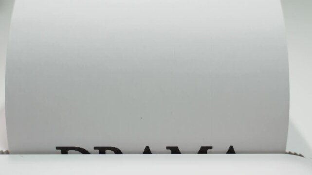 Word drama being typed in bold black letters on white paper close-up