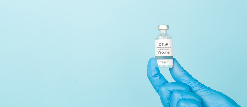 Doctor hand in blue gloves holding DTaP vaccine vial over blue background. DTaP vaccine used to prevent diphtheria, tetanus, and pertussis.