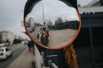 Two men take a selfie reflected in a convex traffic mirror on a city sidewalk. The urban street scene shows parked cars and buildings, suggesting a casual business meeting vibe. © qunica.com
