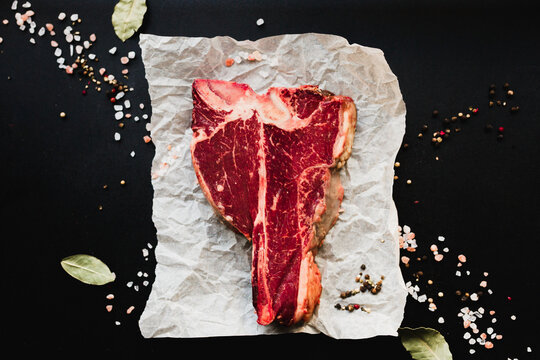 Top view of raw beef t-bone steak with sea salt and peppercorns.