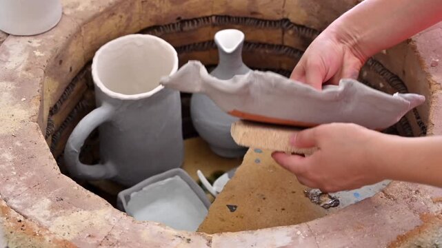 Woman hands arranging clay pottery pieces inside electric kiln for firing process in ceramic studio