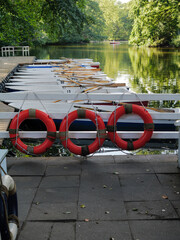 Fototapeta premium Orange Lifebuoy Ring and Rowboats Lined Up Along Wooden Dock Edge