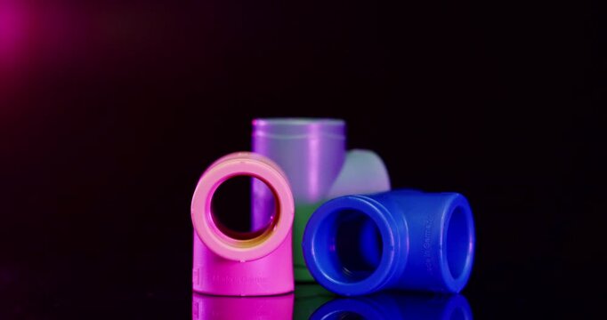 Close up of colorful plastic T-joint pipe fittings and industrial connectors against a dark background with red light