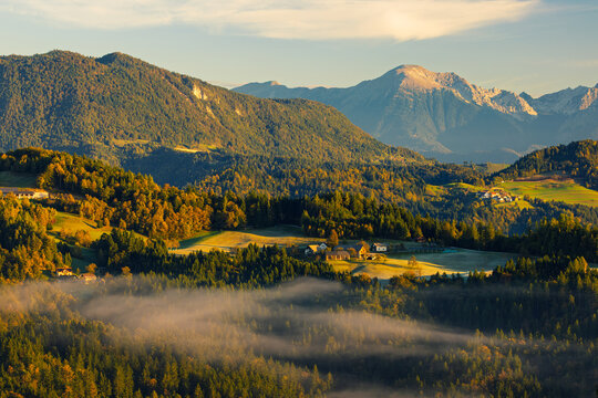 View of radiant sunlight casting shadows over rolling hills and misty valleys, painting the landscape in golden hues and soft blues, Selca, Skofja Loka, Slovenia.