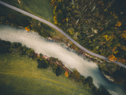 Aerial view of a river flowing through a landscape with contrasting autumn colors and a road running parallel, Bohinjska Bistrica, Radovljica, Slovenia.