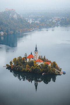 Aerial view of the iconic church on Bled Island, surrounded by the serene lake reflecting the muted autumn colors, Bled, Radovljica, Slovenia.
