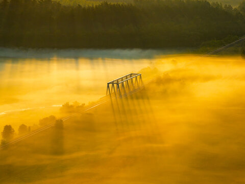 Aerial view of a bridge cutting through a sea of golden fog, sunlight piercing through, creating a dreamy landscape, Motkowice, Swietokrzyskie Voivodeship, Poland.