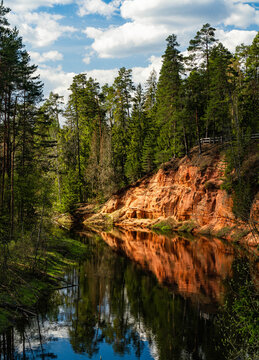 Red sandstone riverbank reflected in a forest river