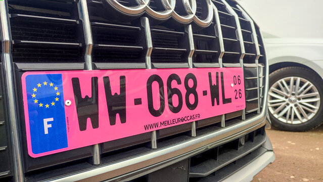 Pink temporary French license plate mounted on the front grille of an Audi car in a parking area.