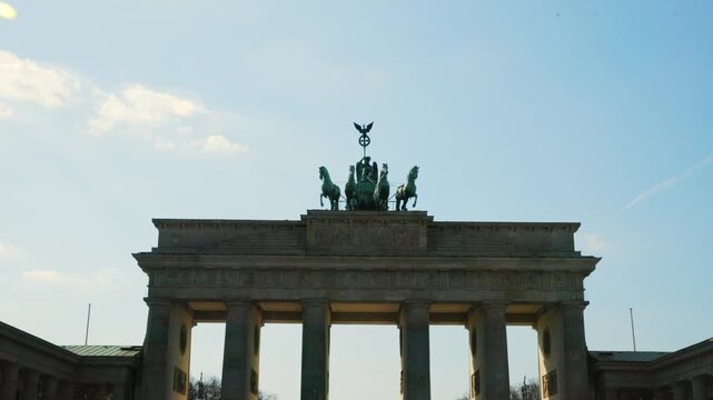 BERLIN, GERMANY - MARCH 23 2026: Panning shot close up of the Quadriga statue on top of the Brandenburg Gate with dramatic sunlight and lens flare in the background
