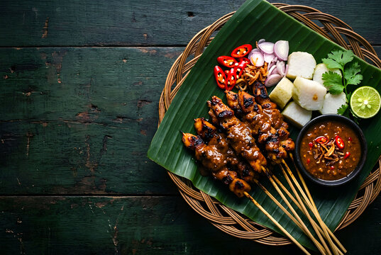Traditional indonesian food, chicken satay (sate ayam) with rice cake,  peanut sauce, sliced chili, chili sambal served in rattan plate on table top with copy space