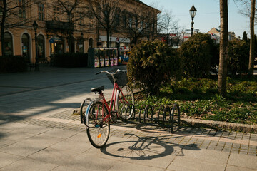 Red bicycle parked near rack in urban square with soft sunlight and shadows in Sombor, Serbia. Concept of sustainable transport, city lifestyle and eco friendly mobility © Ekaterina