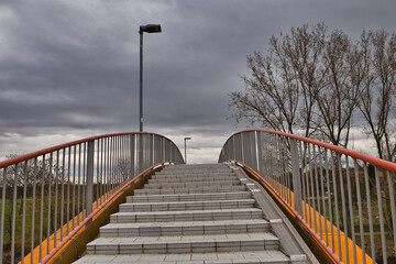 Fototapeta premium Perspektivischer Blick über die Katzenbuckelbrücke in die Saale-Aue bei Leuna, moderne Fußgängerbrücke mit orangefarbenem Geländer, Infrastruktur und Naherholung, Sachsen-Anhalt, Deutschland