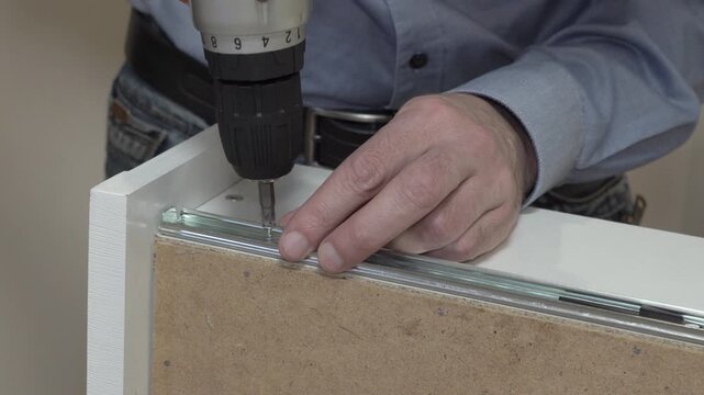 installing drawer guides with screwdriver, Handyman installing metal slides on a wooden drawer
